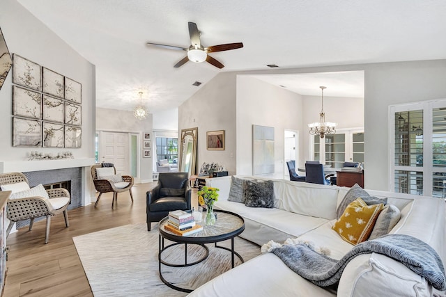 living room with ceiling fan with notable chandelier, high vaulted ceiling, and light hardwood / wood-style flooring