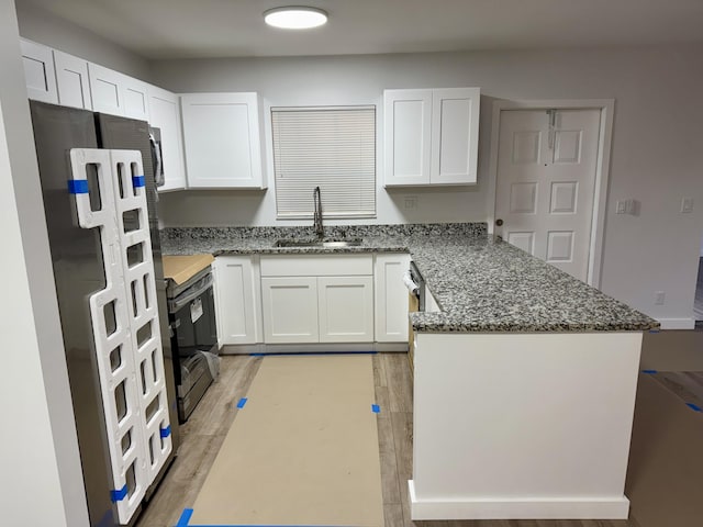 kitchen with sink, white cabinets, dark stone counters, fridge, and range