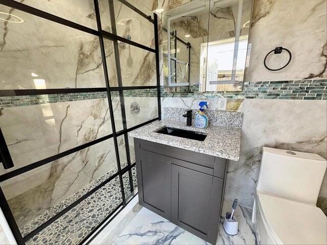 bathroom featuring a shower with door, vanity, tile walls, and toilet