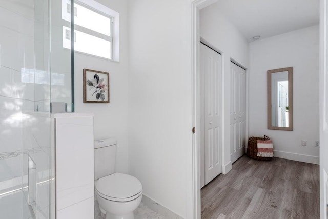 bathroom with baseboards, toilet, wood finished floors, and a shower stall