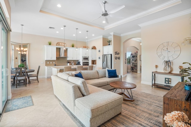 living room featuring crown molding, ceiling fan with notable chandelier, light tile patterned flooring, and a tray ceiling