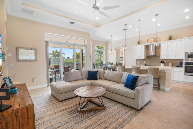 living room with light tile patterned flooring, sink, ornamental molding, a tray ceiling, and ceiling fan