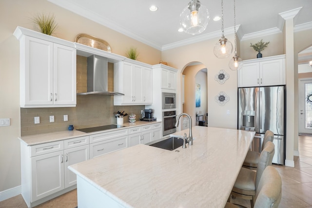 kitchen with white cabinets, stainless steel appliances, a center island with sink, and wall chimney range hood