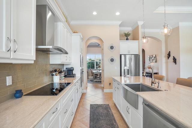 kitchen featuring wall chimney range hood, sink, hanging light fixtures, stainless steel appliances, and white cabinets