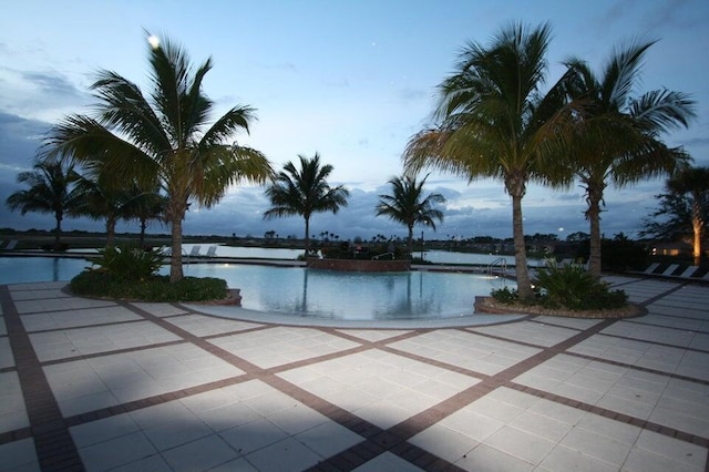 pool at dusk with a patio area and a water view