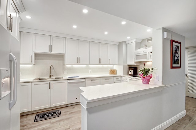 kitchen featuring white cabinetry, sink, white appliances, and kitchen peninsula