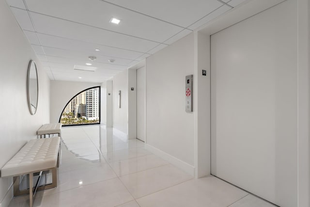 corridor featuring elevator, a paneled ceiling, and light tile patterned floors