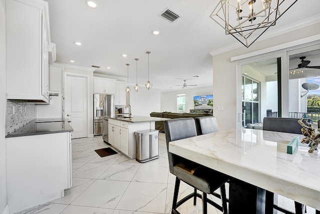 kitchen featuring appliances with stainless steel finishes, decorative light fixtures, an island with sink, white cabinets, and crown molding