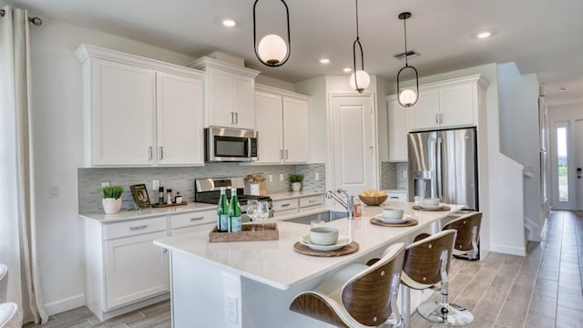 kitchen featuring sink, hanging light fixtures, stainless steel appliances, a kitchen island with sink, and white cabinets