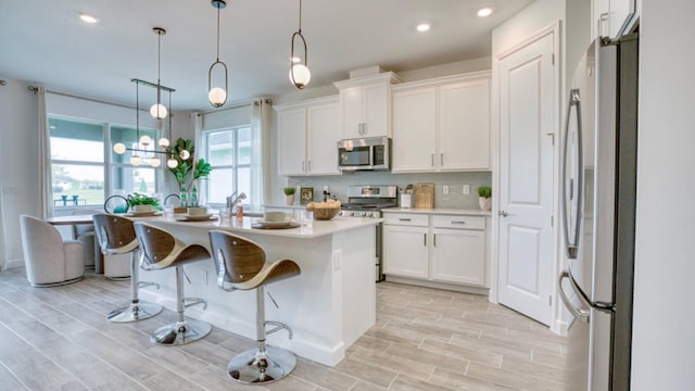 kitchen featuring white cabinetry, appliances with stainless steel finishes, decorative light fixtures, and a center island with sink