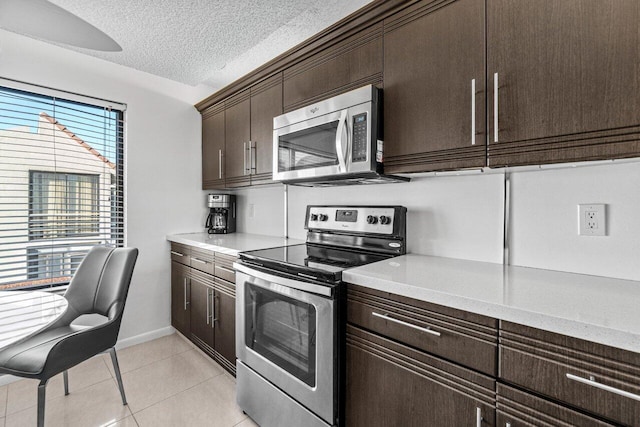 kitchen featuring dark brown cabinetry, a textured ceiling, light tile patterned floors, appliances with stainless steel finishes, and pendant lighting