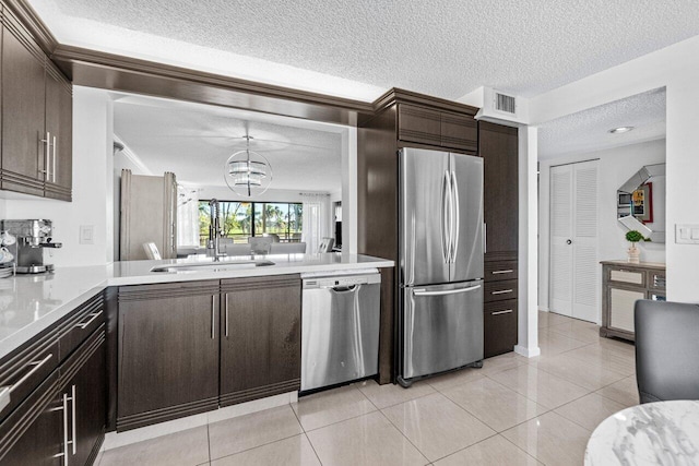 kitchen with sink, light tile patterned floors, stainless steel appliances, dark brown cabinetry, and decorative light fixtures