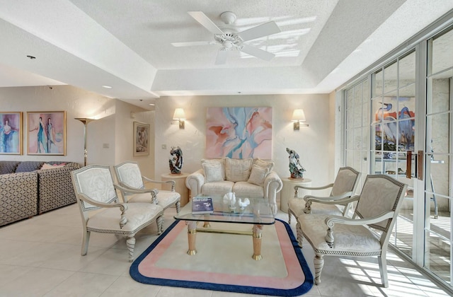 living room with ceiling fan, a tray ceiling, a textured ceiling, and light tile patterned floors