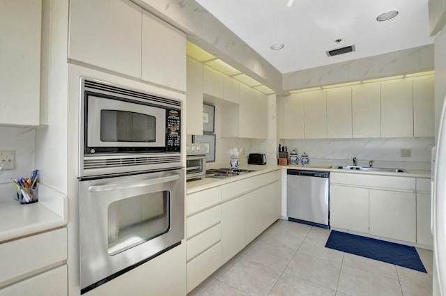 kitchen with tasteful backsplash, sink, white cabinets, light tile patterned floors, and stainless steel appliances