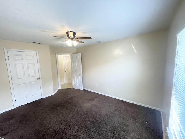 unfurnished bedroom with ceiling fan and dark colored carpet