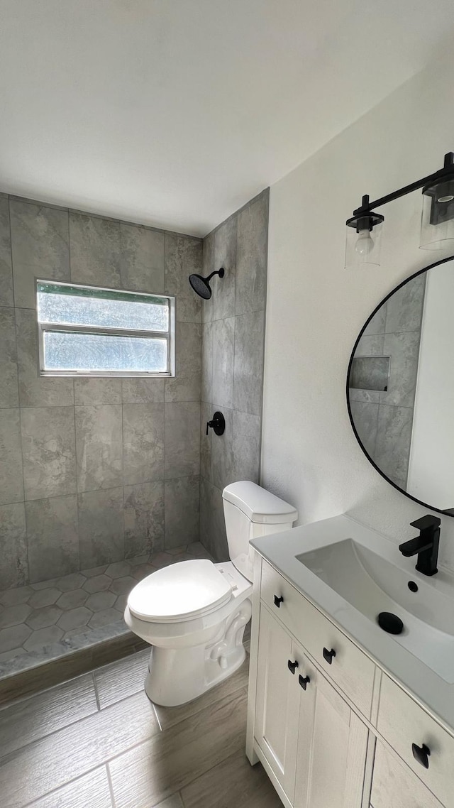 bathroom featuring a tile shower, vanity, wood-type flooring, and toilet