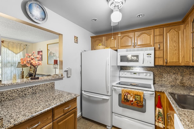 kitchen with sink, light tile patterned floors, white appliances, light stone countertops, and decorative backsplash