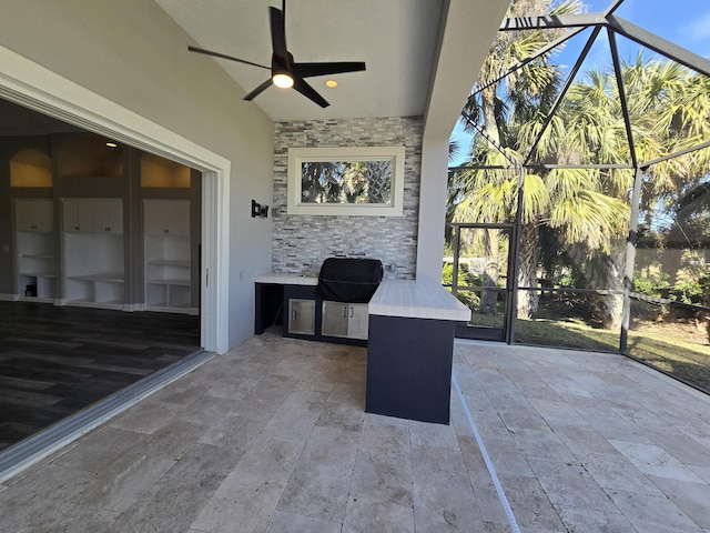 view of patio / terrace featuring exterior kitchen, area for grilling, ceiling fan, and glass enclosure