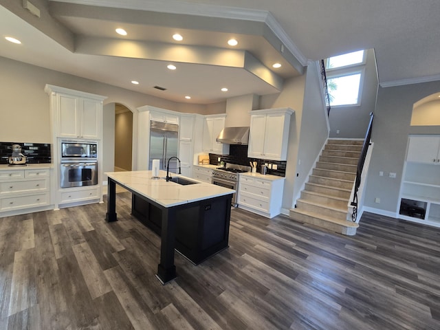 kitchen featuring sink, white cabinets, ornamental molding, built in appliances, and a center island with sink