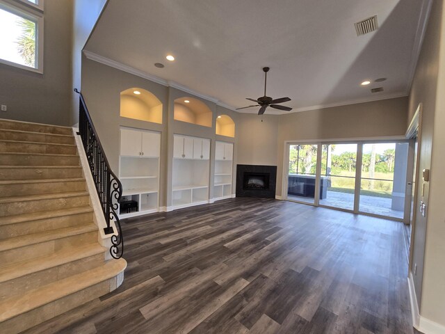 unfurnished living room with built in shelves, dark wood-type flooring, ornamental molding, and ceiling fan