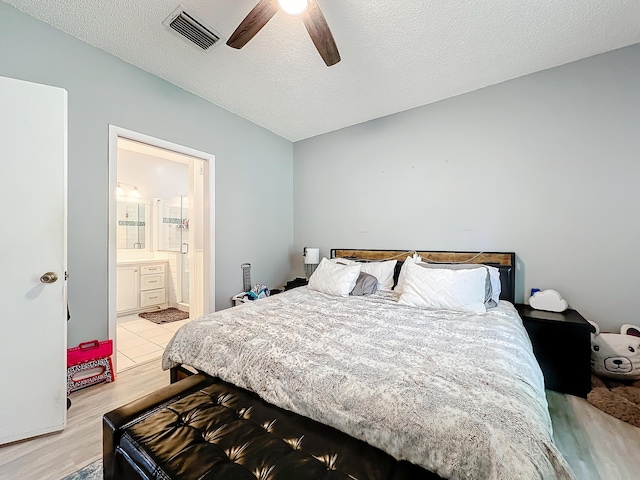 bedroom featuring ceiling fan, ensuite bath, light hardwood / wood-style floors, and a textured ceiling