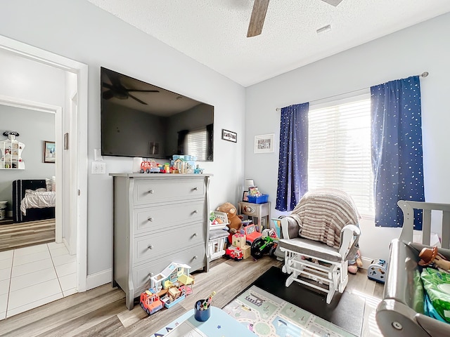 playroom with a textured ceiling, ceiling fan, and light wood-type flooring