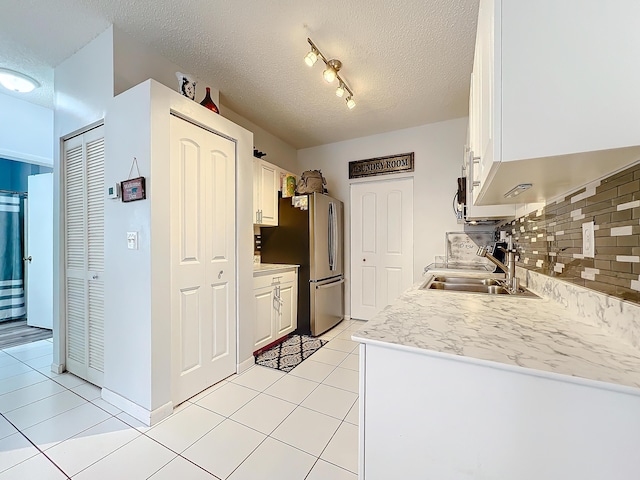 kitchen featuring sink, backsplash, a textured ceiling, white cabinets, and light tile patterned flooring