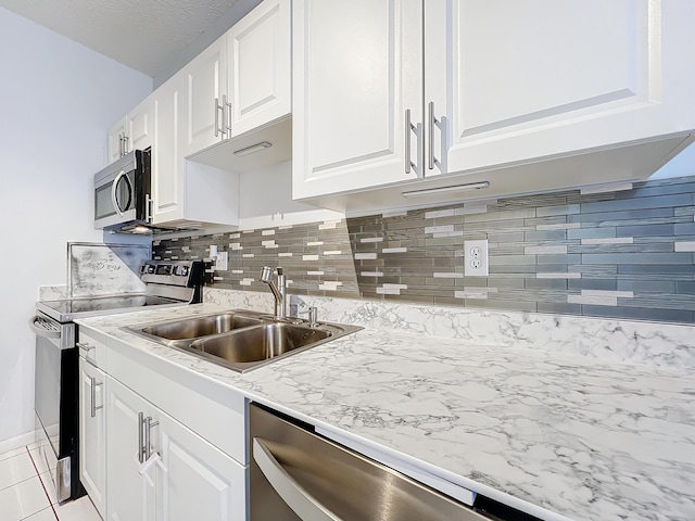 kitchen featuring light tile patterned flooring, appliances with stainless steel finishes, sink, white cabinets, and decorative backsplash