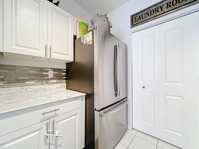 kitchen featuring white cabinetry, backsplash, stainless steel fridge, light tile patterned floors, and a textured ceiling