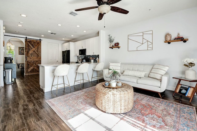 living room featuring ceiling fan, a barn door, dark hardwood / wood-style flooring, and sink