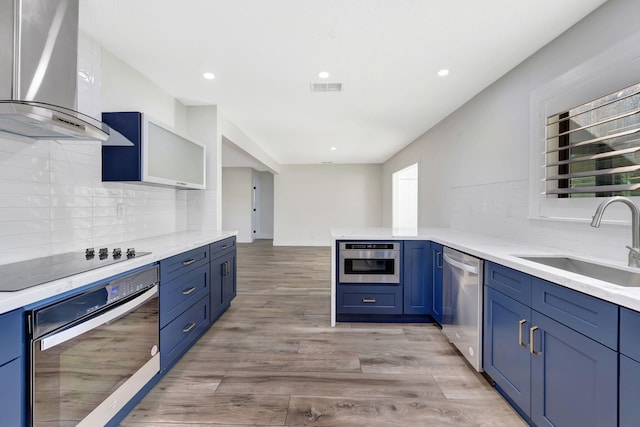 kitchen featuring wall chimney exhaust hood, sink, light wood-type flooring, appliances with stainless steel finishes, and kitchen peninsula