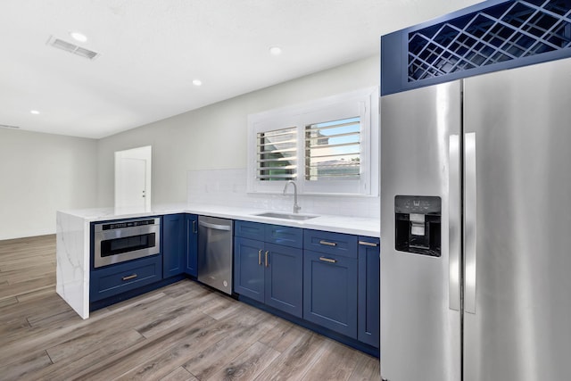 kitchen featuring sink, light hardwood / wood-style flooring, appliances with stainless steel finishes, blue cabinets, and decorative backsplash