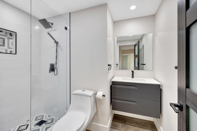 bathroom featuring vanity, tiled shower, hardwood / wood-style floors, and toilet