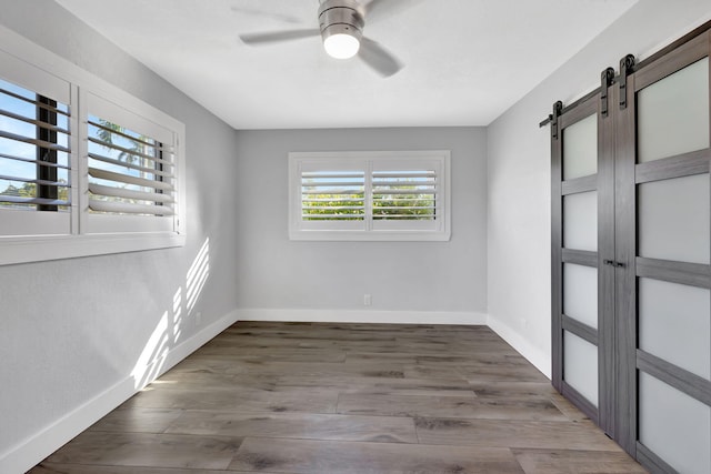 empty room with a barn door, hardwood / wood-style floors, and ceiling fan