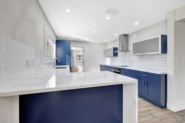 kitchen featuring wall chimney range hood, sink, oven, light stone countertops, and kitchen peninsula