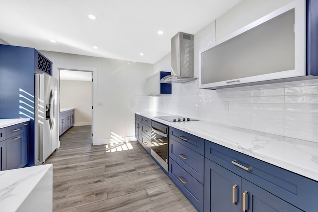 kitchen featuring light stone counters, wall chimney range hood, decorative backsplash, and appliances with stainless steel finishes