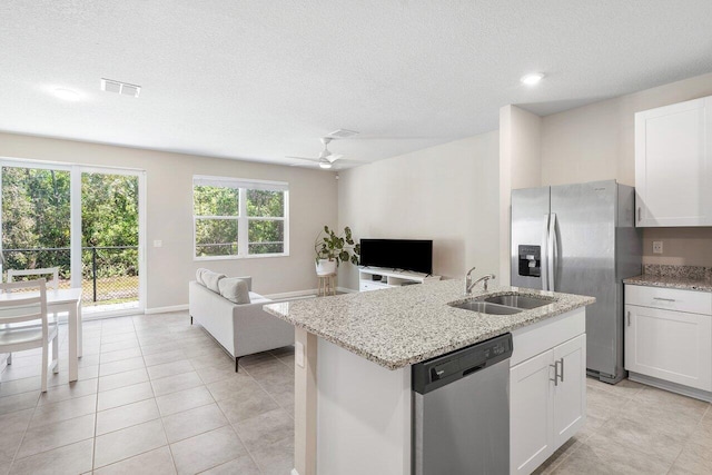 kitchen with sink, appliances with stainless steel finishes, white cabinetry, light stone countertops, and a center island with sink