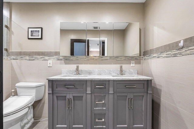 bathroom featuring toilet, double vanity, tile walls, and a sink