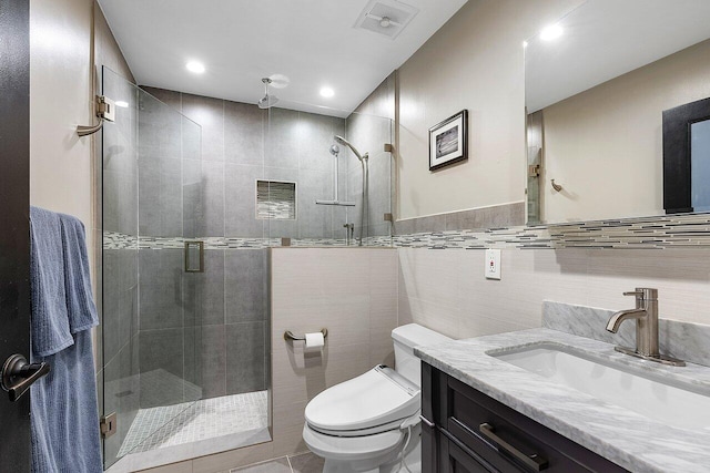 bathroom featuring a stall shower, vanity, toilet, and tile walls