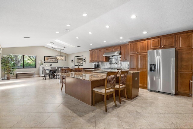 kitchen featuring a spacious island, vaulted ceiling, stainless steel fridge, under cabinet range hood, and a kitchen breakfast bar