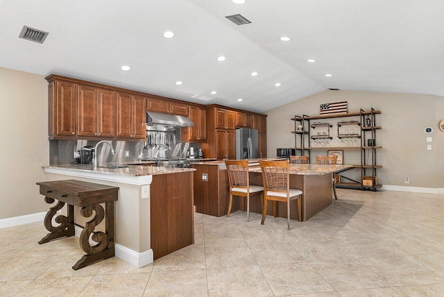 kitchen featuring a breakfast bar area, stainless steel fridge, visible vents, and under cabinet range hood