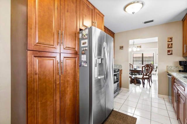 kitchen with stainless steel appliances, an inviting chandelier, light tile patterned floors, and light stone counters