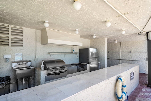 kitchen featuring stainless steel refrigerator, range hood, and a textured ceiling