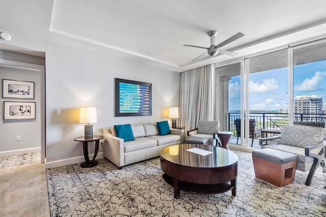 living room with a tray ceiling, ceiling fan, and a wall of windows