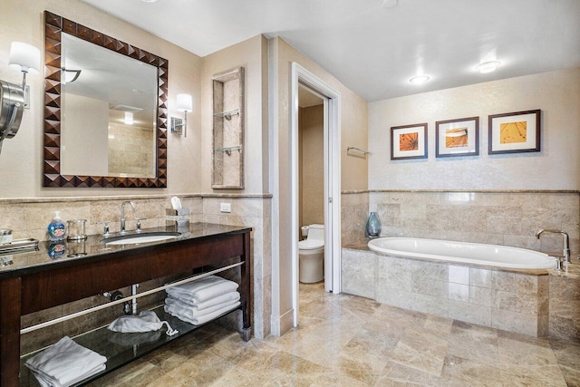 bathroom with vanity, tiled bath, and toilet