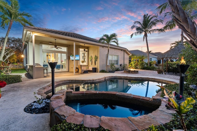 view of pool featuring an in ground hot tub, ceiling fan, exterior bar, a fire pit, and a patio