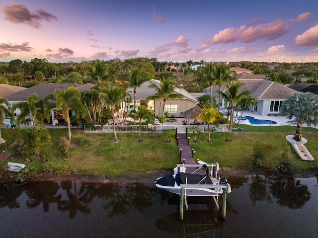 back house at dusk featuring a water view and a lawn