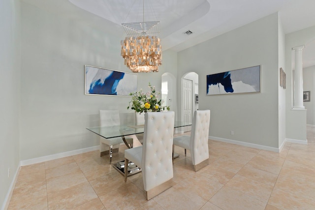 tiled dining space featuring a notable chandelier, a raised ceiling, and ornate columns