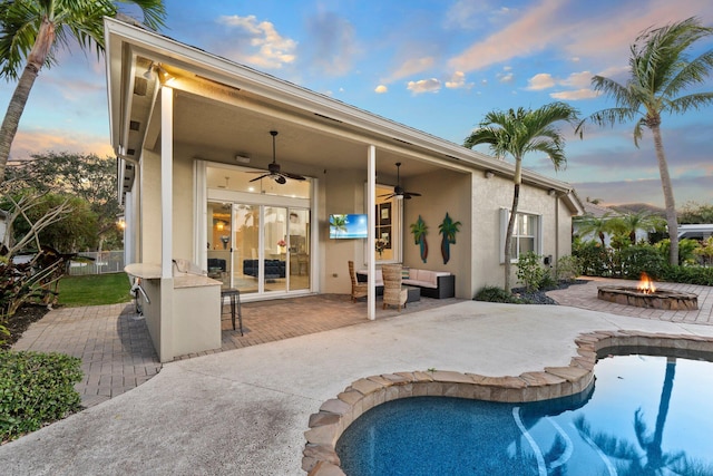 back house at dusk featuring exterior bar, a patio area, ceiling fan, and an outdoor fire pit