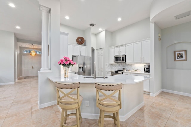 kitchen featuring sink, a breakfast bar, appliances with stainless steel finishes, white cabinets, and ornate columns